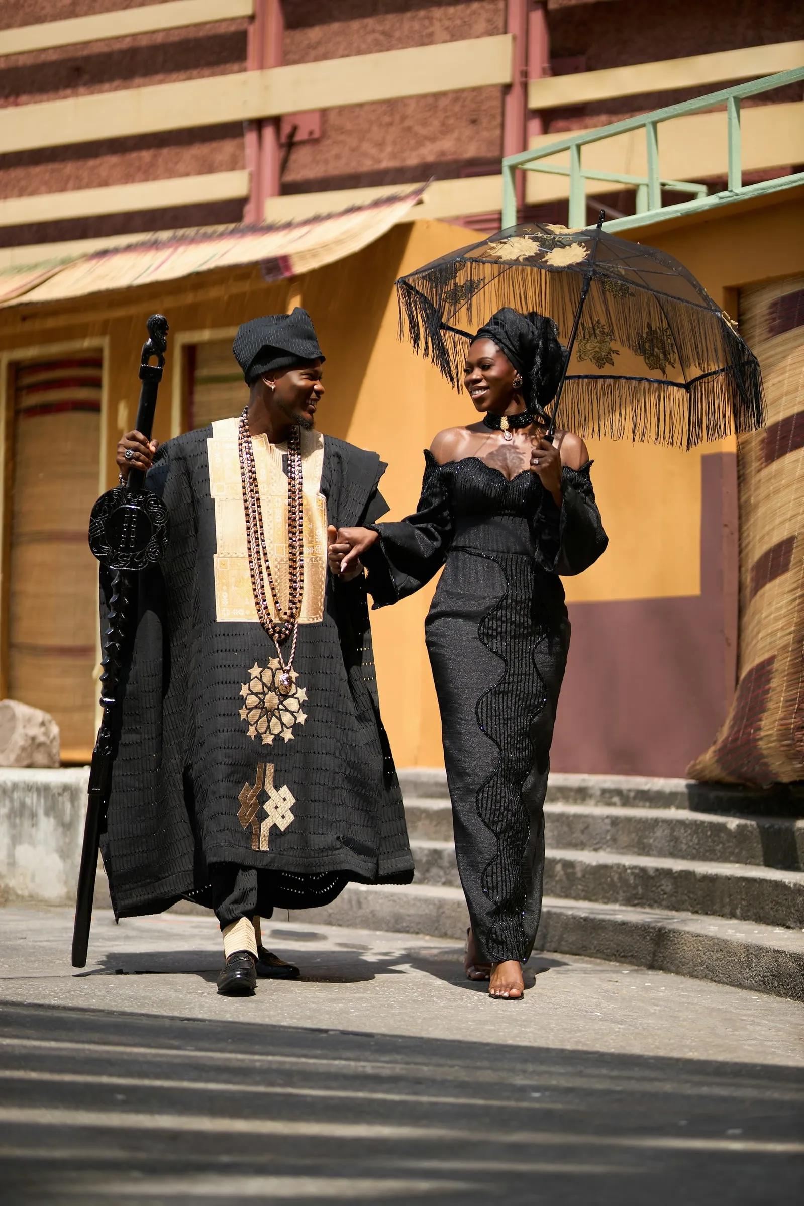 Couple in traditional attire walking down the steps under a parasol