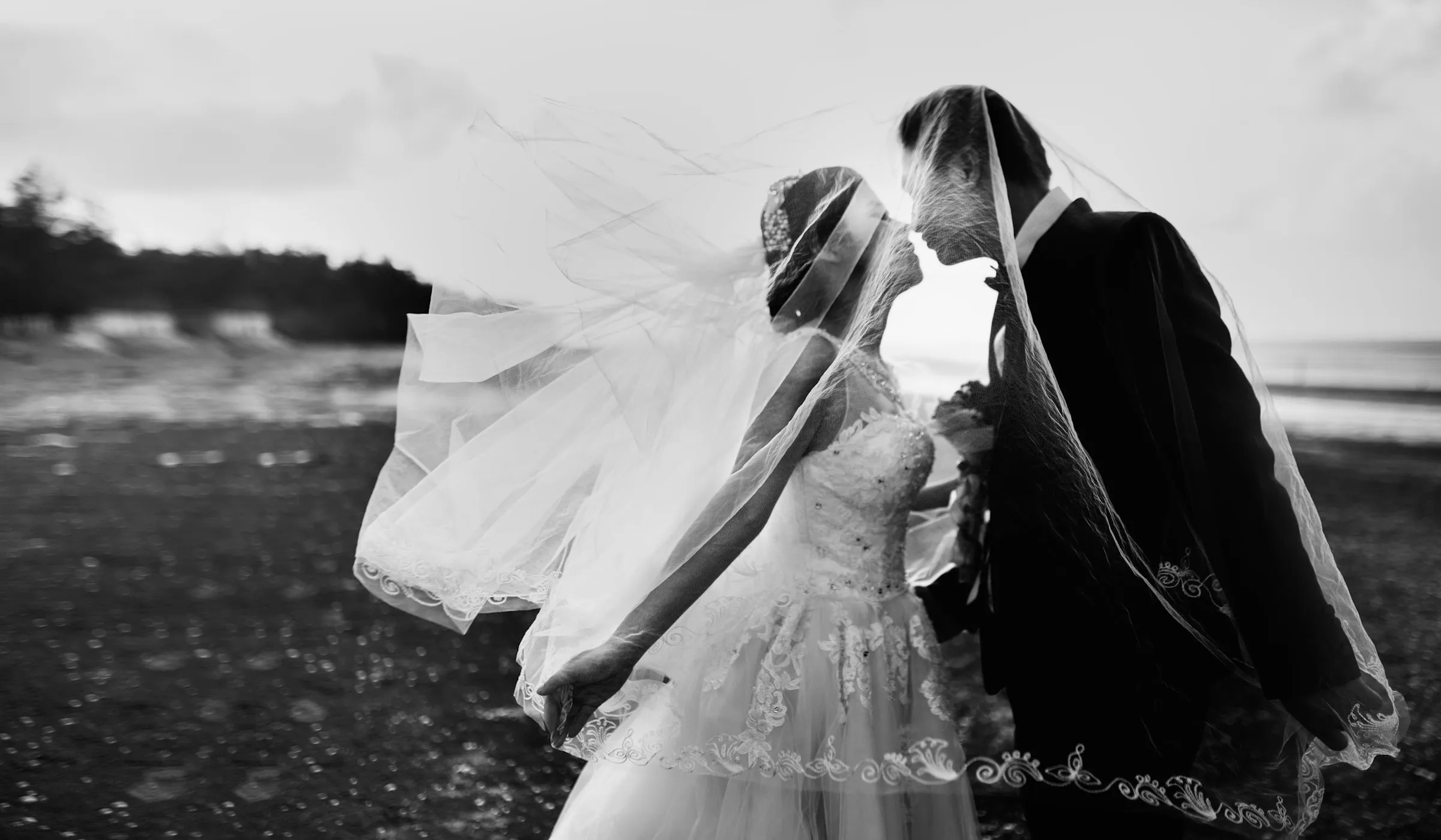 Les mariés s’embrassent, le voile soulevé par le vent, en noir et blanc