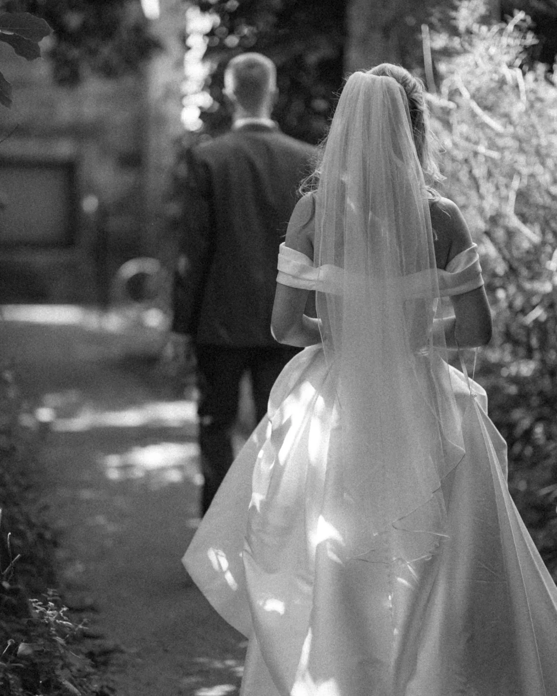 The bride and her veil from behind, in a shaded alley, black and white